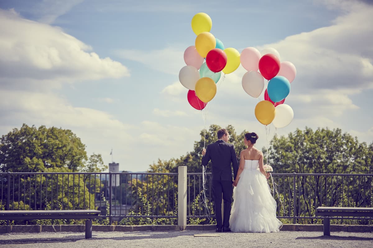 Brautpaar mit bunten Luftballons an einem Aussichtsgeländer, im Hintergrund die Sparrenburg in Bielefeld