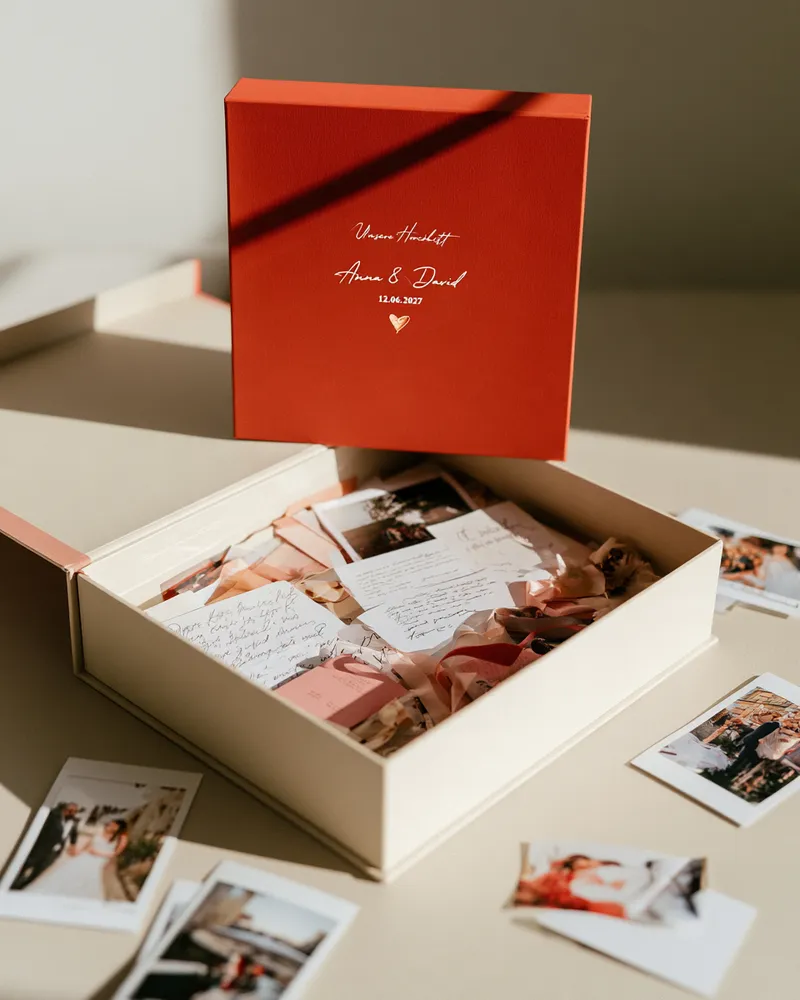 Personalisierte Erinnerungsbox mit Namen und Hochzeitsdatum, darin gesammelte Sofortbilder, handgeschriebene Briefe und Trockenblumen