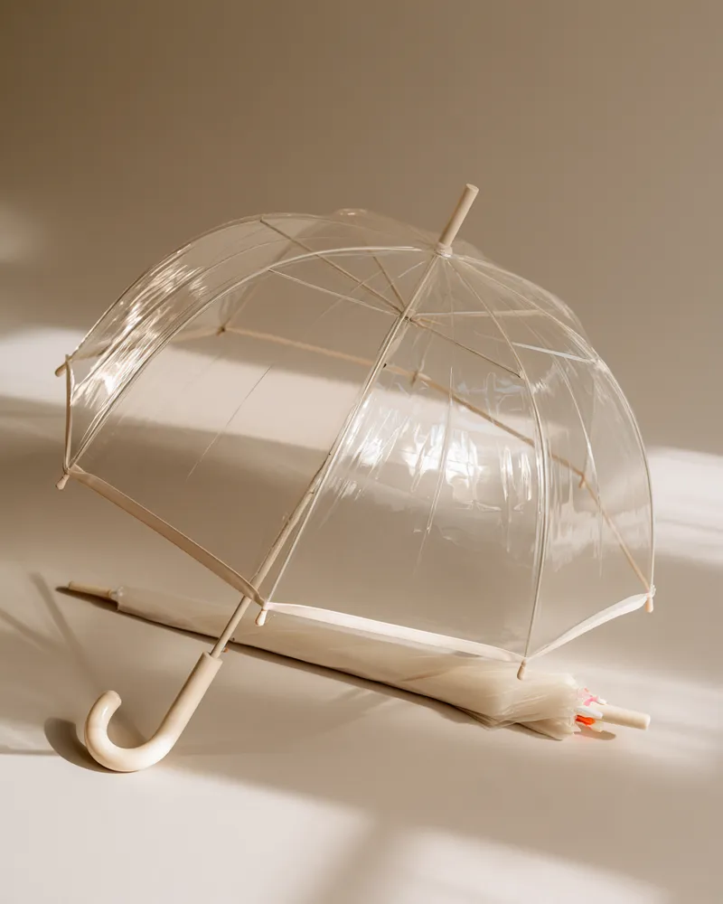 Transparenter Glockenschirm mit cremefarbenem Rundgriff – ein Brautschirm, der Kleid und Frisur bei Regen am Hochzeitstag schützt